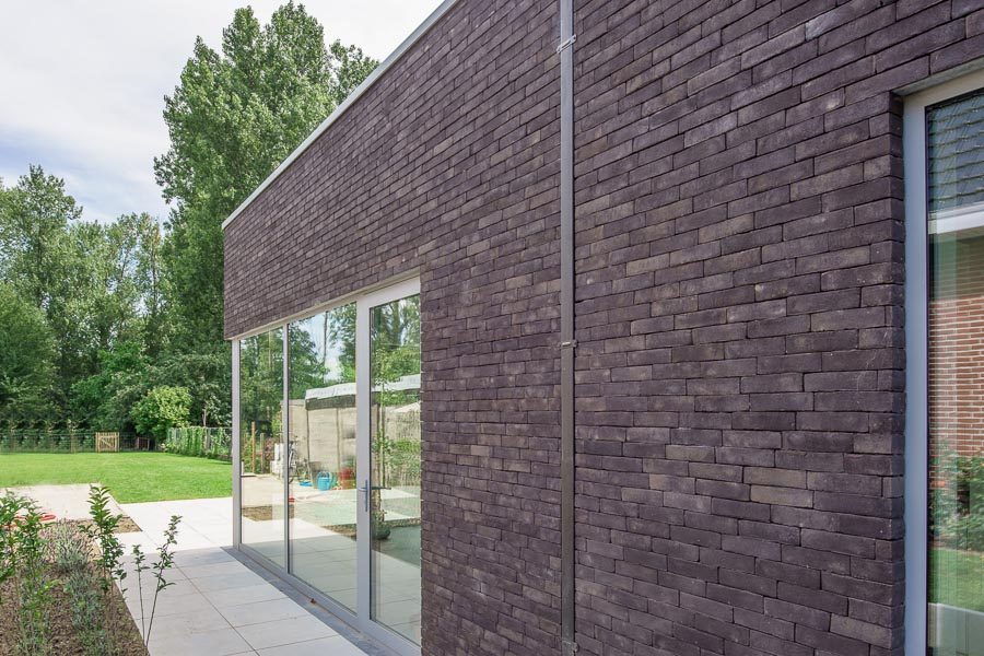 Donkere voegloze gevel van moderne woning met grote ramen en tuin