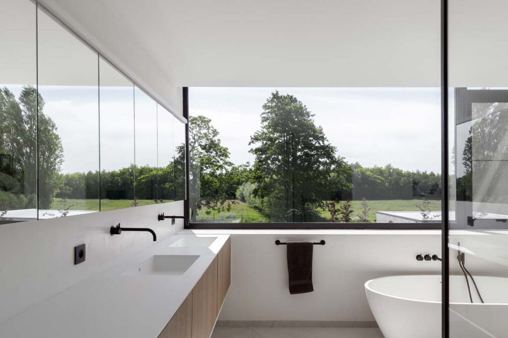Moderne badkamer afwerking met dubbele wastafel en groot raam met uitzicht op tuin