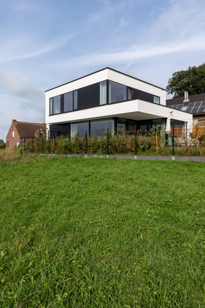Witte kubuswoning met zwarte details en grote glaspartijen aan de tuinzijde