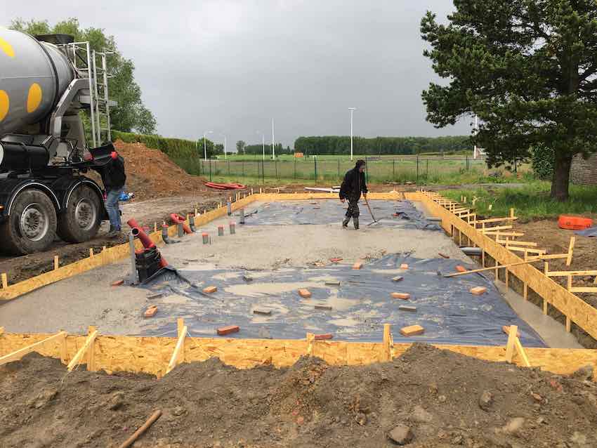 Een betonnen funderingsplaat wordt tijdens de bouwfase gestort met vooraf geplaatste leidingen en rioleringsaansluitingen.