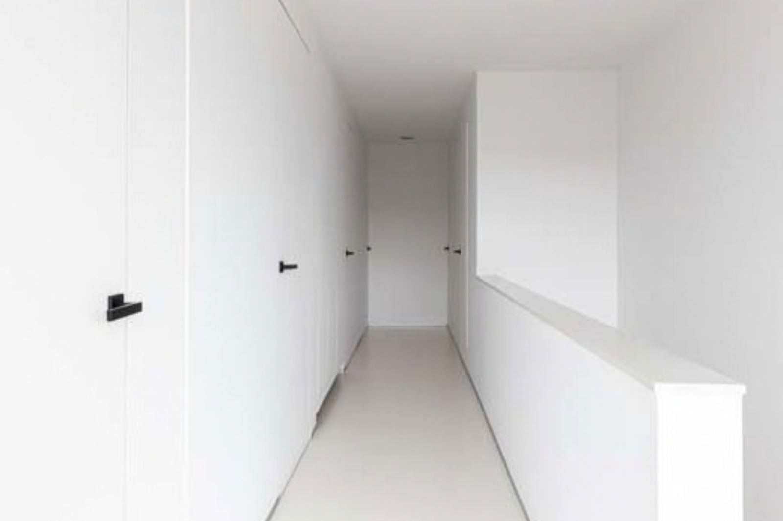 Lichte gang met een naadloze witte gietvloer en strakke witte deuren in een moderne woning.