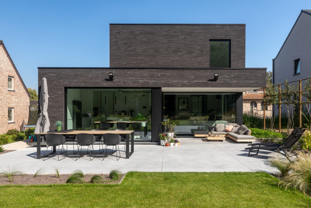 Moderne woning met donkere gevelsteen en ingericht terras in het eerste jaar na de oplevering.